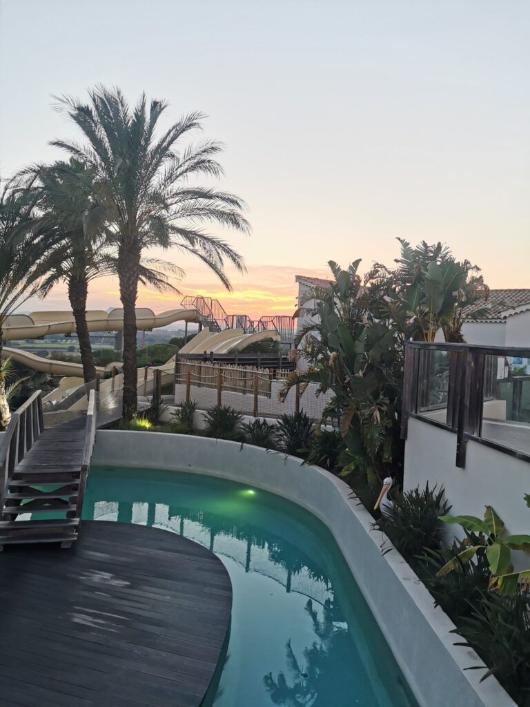 Sunset over Eurocamp French Riviera - Club Colombier campsite pool with palm trees and water slides.