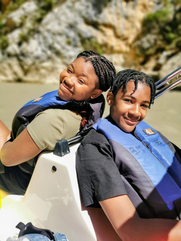 Two children smiling back to back on a pedal boat on Lac de Sainte -Croix with turquoise water around them