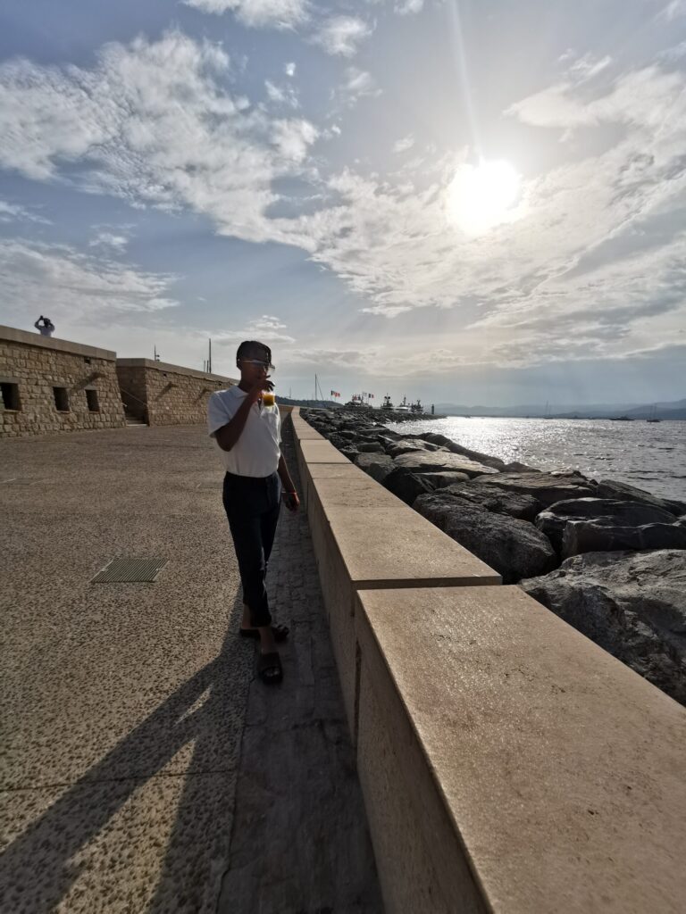 Boy walking along the harbour wall in Saint Tropez on a sunny afternoon with the Mediterranean sea beside him.