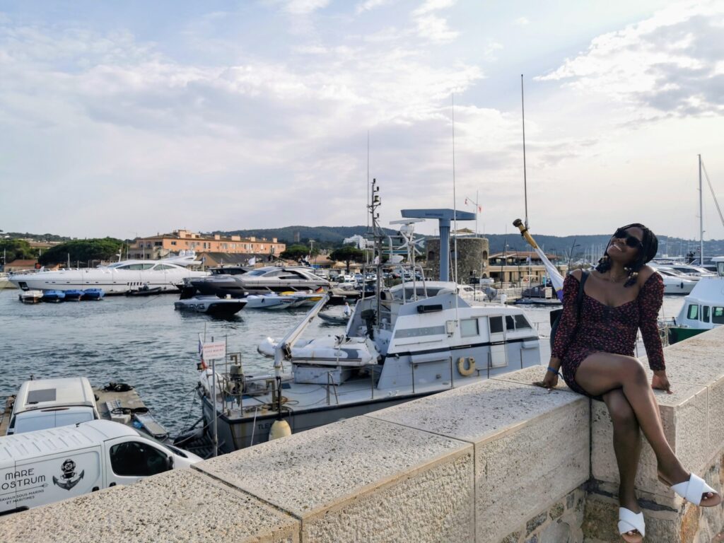 Woman in red dress sitting on the harbour wall overlooking the Mediterranean sea in Saint Tropez on the French Riviera.