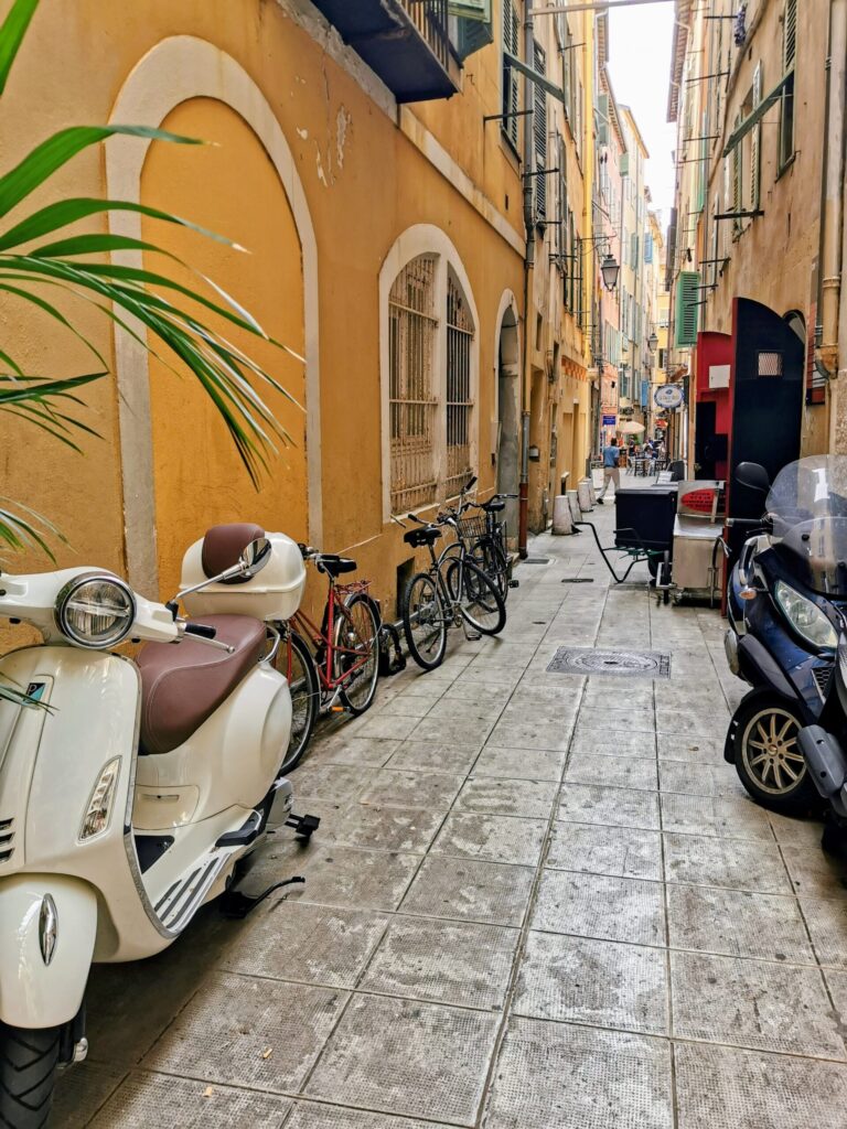 Narrow colourful street in Nice Old Town with scooters and bicycles parked along the walls.