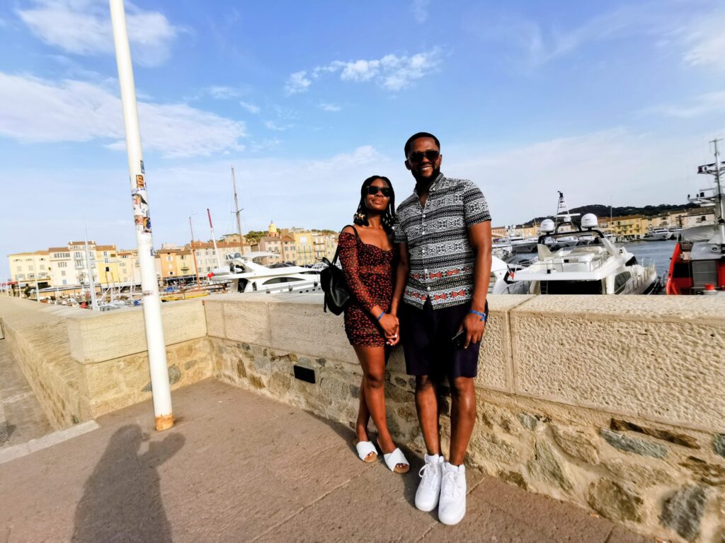 Couple standing by the harbour in Saint Tropez with yahts and pastel buildings in the background.