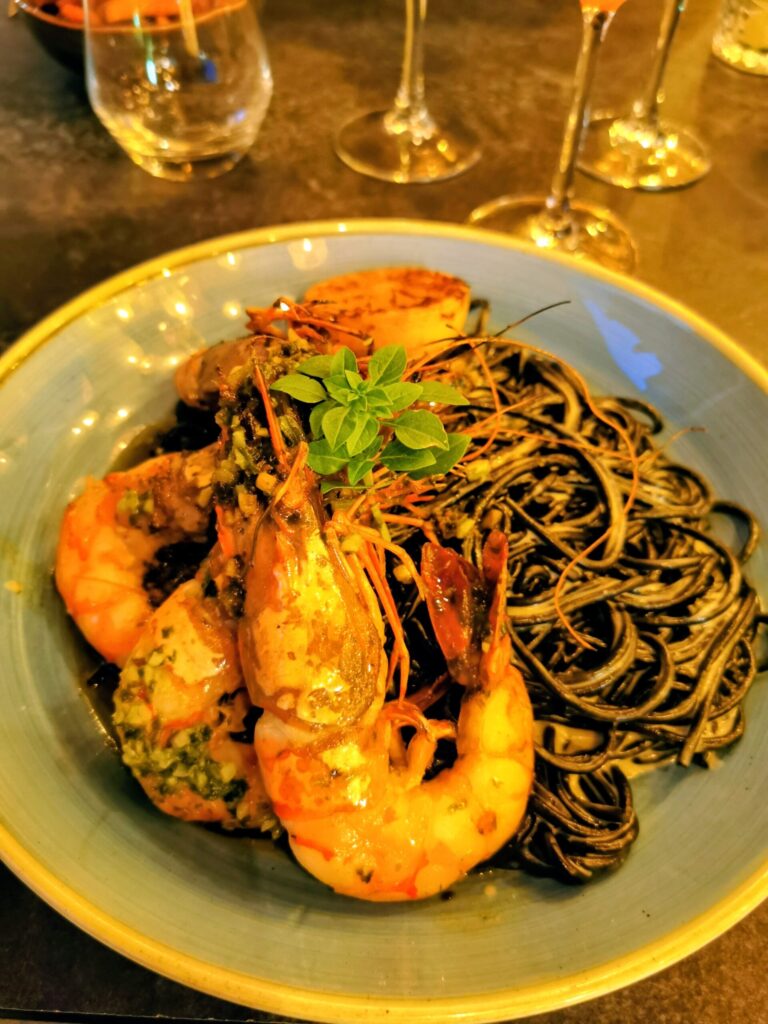 Seafood pasta with Prawns and black Spaghetti served in a restaurant with wine glasses on the table.