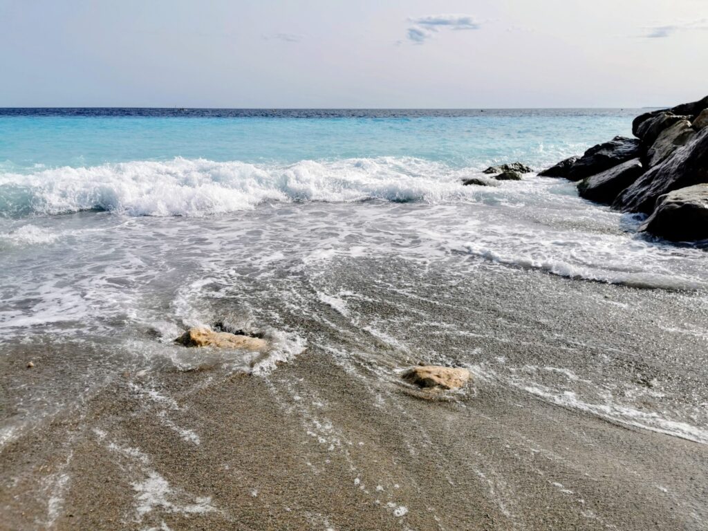 Waves rolling onto a pebble beach in Nice with clear blue water and rocky shoreline.
