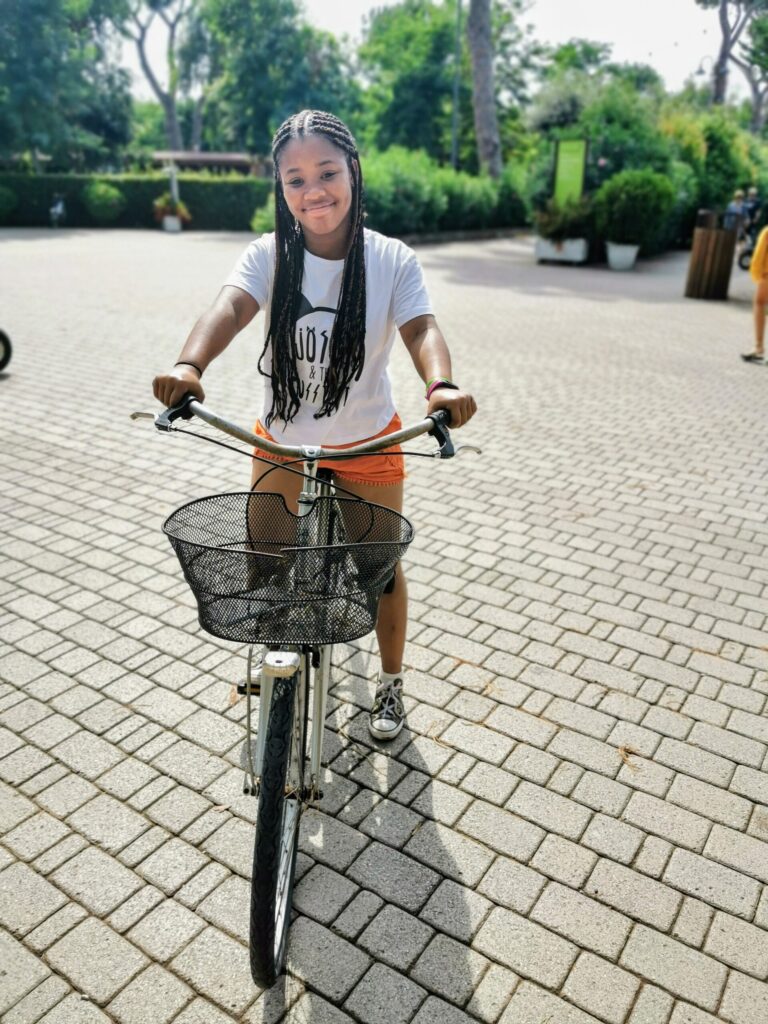 Teenage girl riding a bike through a tree-lined Eurocamp campsite in the summer. 