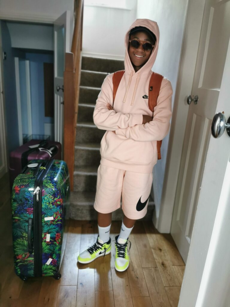 Teenage boy standing beside a suitcase at home before a family trip.