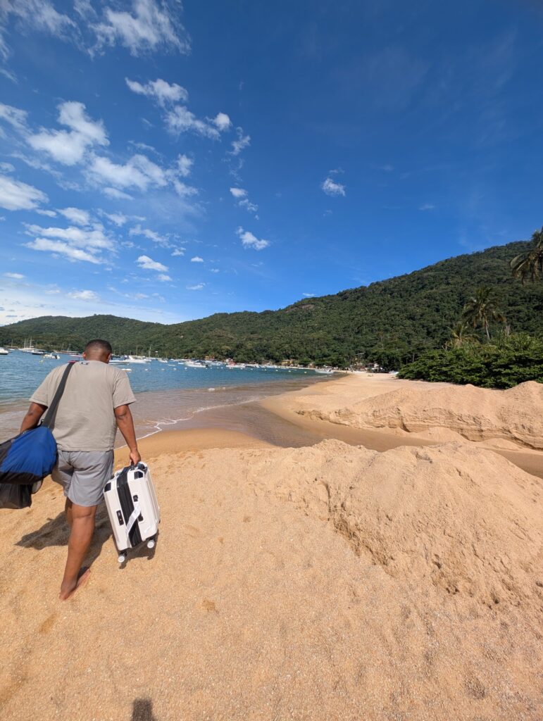 Man walking along the beach on Ilha Grande, Brazil, carrying a suitcase.